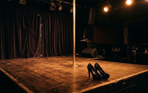 Empty club stage with pole and platform heels — a quiet moment that captures the reality of exotic dancer burnout on tour